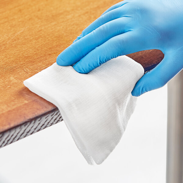 A hand in a blue glove using a 3M tack cloth to clean a table.