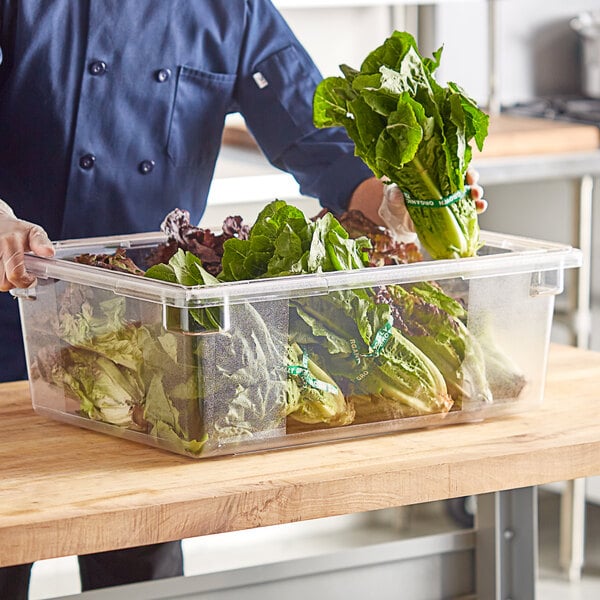 A man in a chef's uniform holding a Choice clear polycarbonate food storage box filled with vegetables.