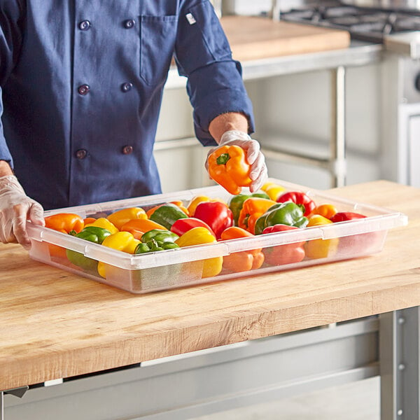 A person holding a clear polycarbonate food storage box filled with yellow and red bell peppers.