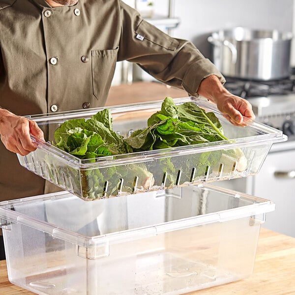 A person holding a Choice clear polycarbonate food box drain tray filled with lettuce.