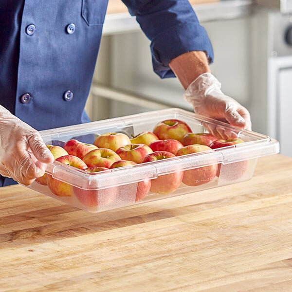 A hand holding a clear polycarbonate food storage box full of apples.