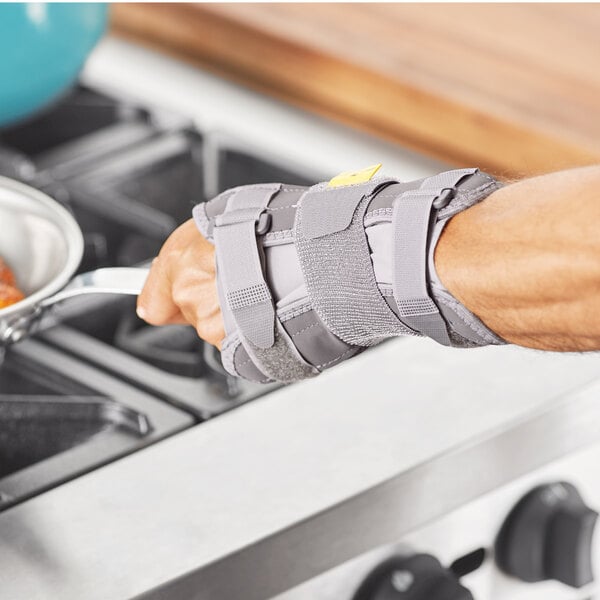 The left wrist of a person wearing a 3M Futuro Deluxe wrist stabilizer using a pan on a stove.