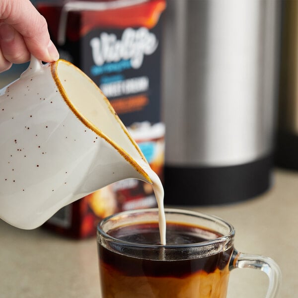 A person pouring Violife Seductive Caramel Coffee Creamer into a cup of coffee.