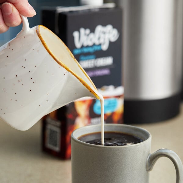 A hand pours Violife Supreme Plant-Based Vegan Sweet Cream Boldly Original Coffee Creamer into a cup of coffee.