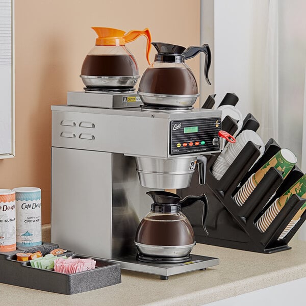 A Curtis commercial coffee maker on a counter with coffee cups underneath.