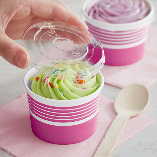 A hand holding a pink paper cup filled with frozen yogurt with a wooden spoon.