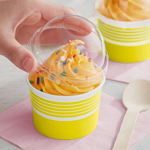 A hand holding a plastic lid over a yellow Choice paper cup of frozen yogurt with sprinkles.