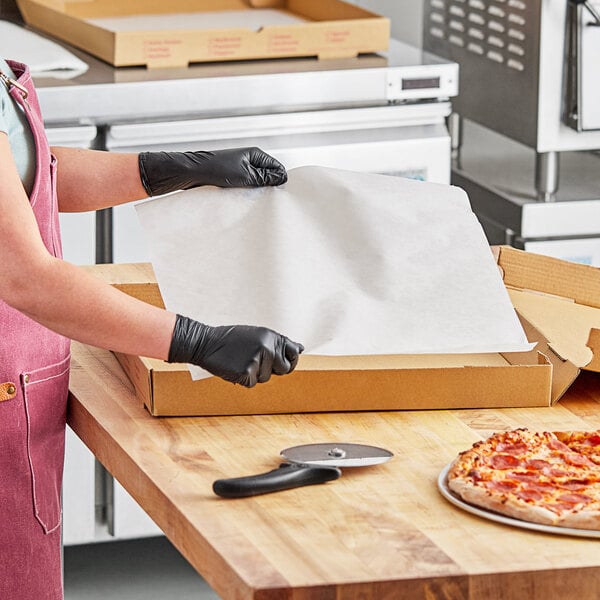 A person in a black apron and gloves using a pizza cutter on a pizza on a counter.