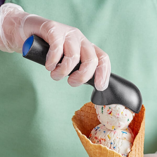 A hand in a blue plastic glove holding a blue ice cream scoop with a scoop of ice cream.