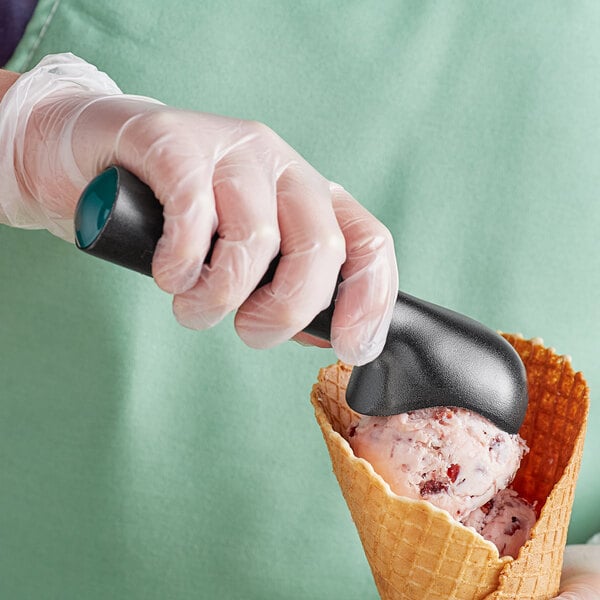 A hand in a black glove holding a green Choice #16 ice cream scoop filled with ice cream.