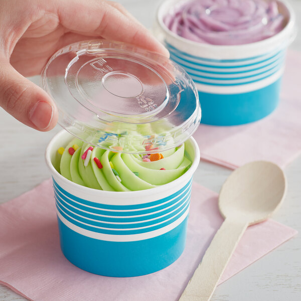 A hand holding a wooden spoon in a blue paper cup with a scoop of ice cream in it.