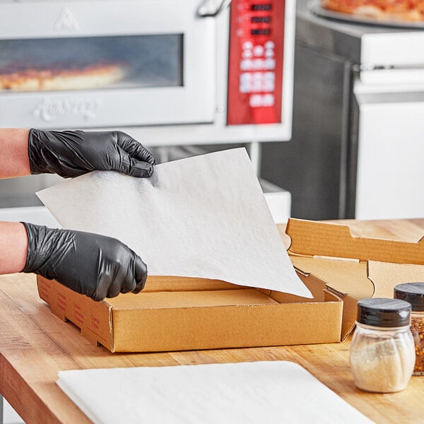 A person wearing black gloves is putting a Quilon coated paper on a pizza box.