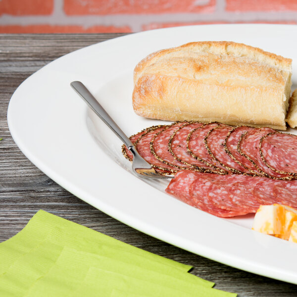 A 10 Strawberry Street white porcelain oval platter with slices of meat, a bread roll, and a knife on a table.