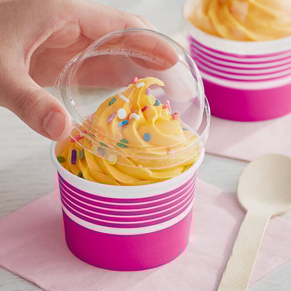 A hand holding a Choice pink and white paper cup of frozen yogurt with a plastic lid over it.