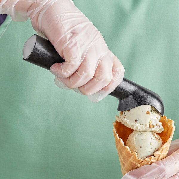 A person in a gloved hand using a Choice #24 silver ice cream scoop to put white ice cream in a waffle cone.