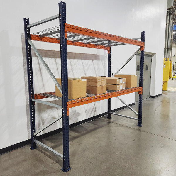 A blue and orange Interlake Mecalux heavy-duty bolted pallet rack with wire deck shelves holding boxes.