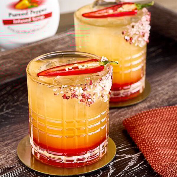 Two glasses of orange and yellow drinks with Real Pepper Puree Infused Syrup with a slice of pepper on top.