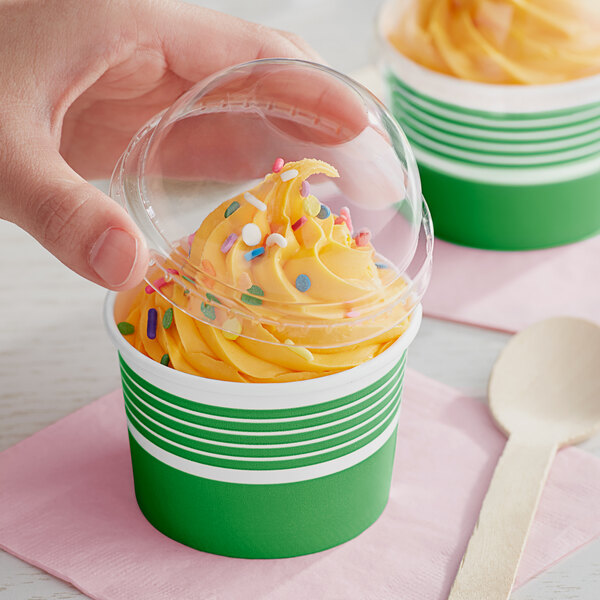 A hand holding a green and white Choice paper cup of frozen yogurt with a plastic lid and sprinkles.