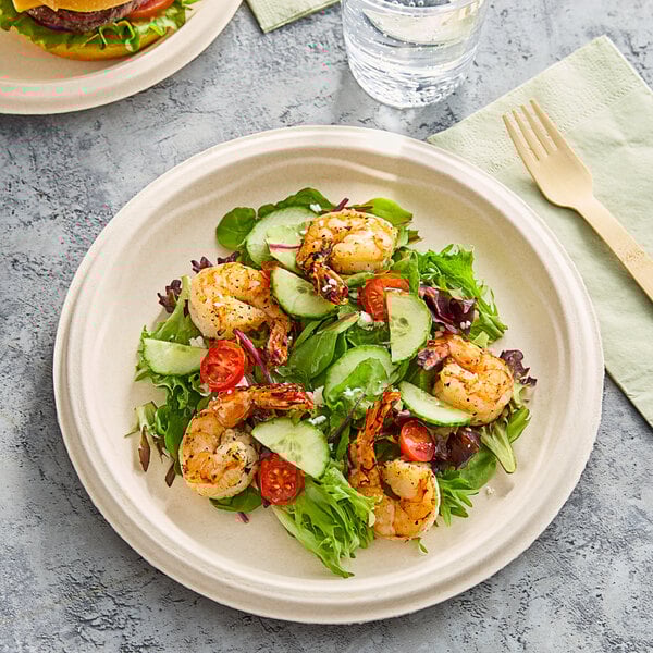 A Dart ProPlanet fiber plate with a shrimp salad and a hamburger on a table with a wooden fork.