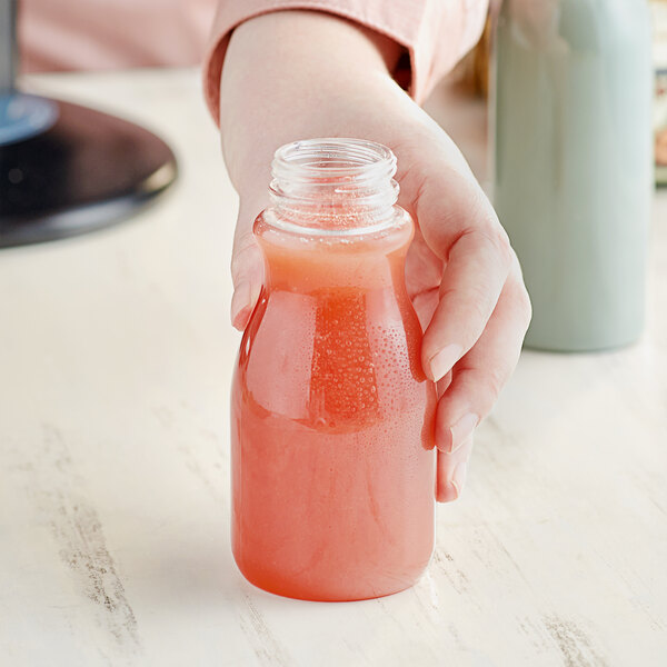 A hand holding an 8 oz. round clear PET juice bottle full of pink liquid.