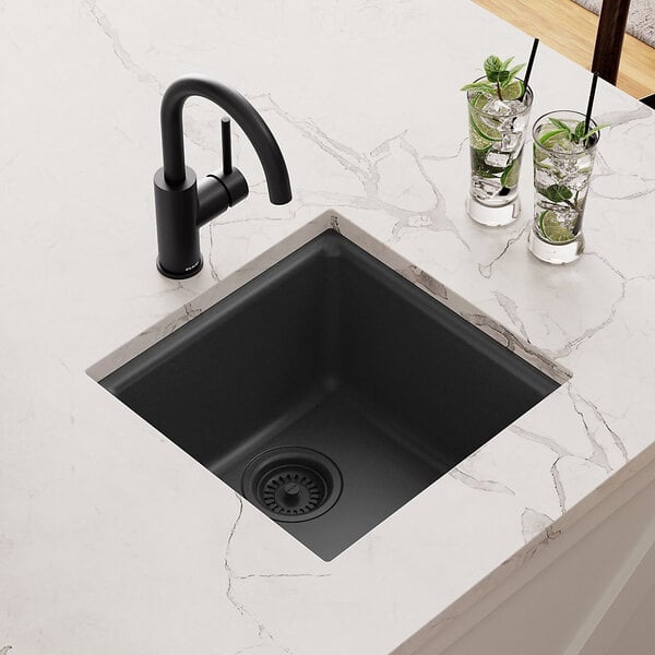 A Zurn Elkay matte black Quartz bar sink on a marble counter with glasses of ice and lime slices.