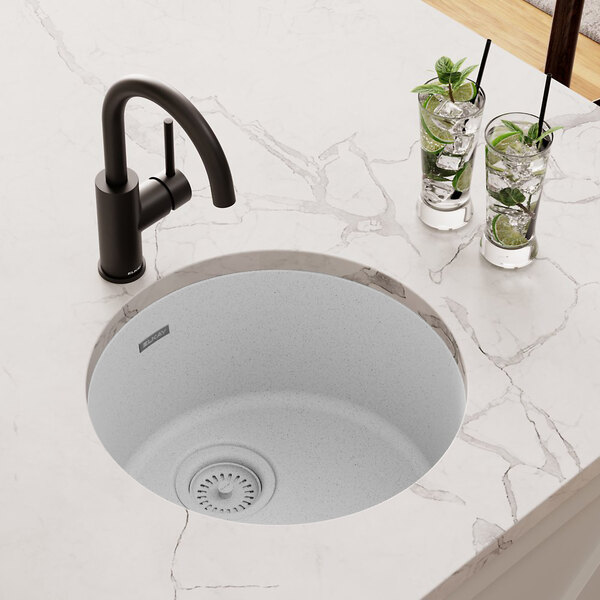 A Zurn Elkay white quartz sink with two glasses of ice and a black faucet above it.