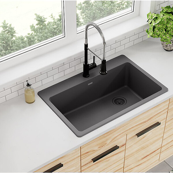 A Zurn Elkay Dusk Gray Quartz sink with a faucet on a counter with a plant in a window.