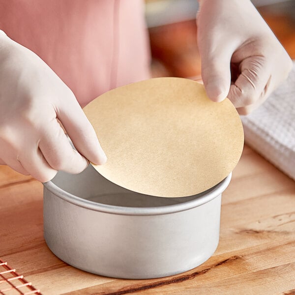 A person using Baker's Lane Quilon-coated parchment pan liner to line a round metal pan.