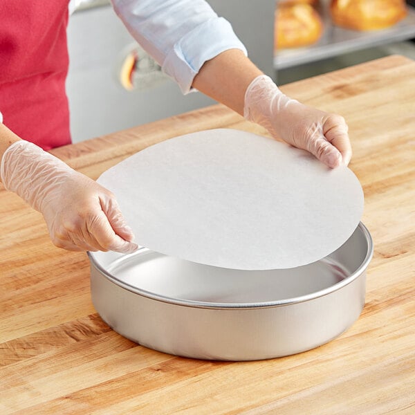 A person in gloves placing a Baker's Lane Quilon-coated parchment liner in a round metal pan.