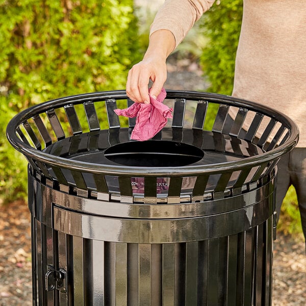 A woman using a pink cloth to clean a black Lancaster Table & Seating trash can.