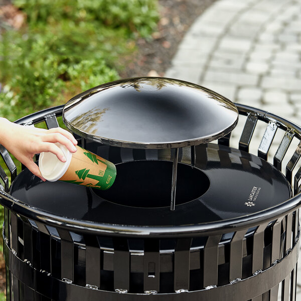A hand putting a coffee cup into a Lancaster Table & Seating black steel rain bonnet lid on a trash can.
