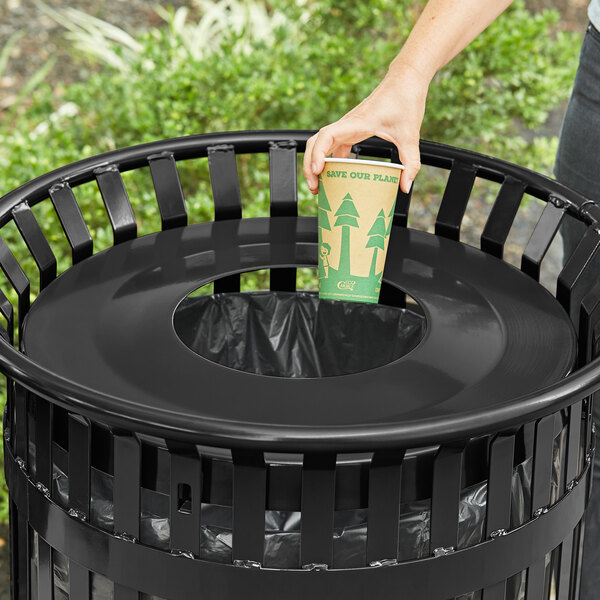 A hand putting a cup into a Lancaster Table & Seating black round flat lid for a trash can.