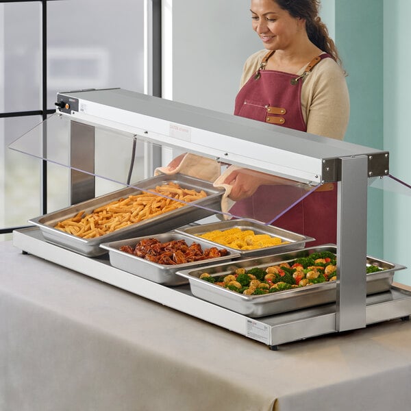 A woman in a red apron putting food into a ServIt buffet warmer on a counter.
