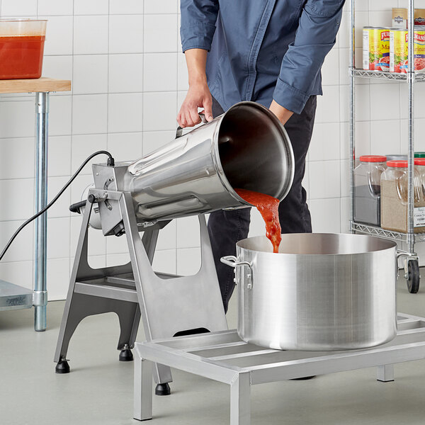 A man pouring red sauce from an Avamix electric blender into a large pot.