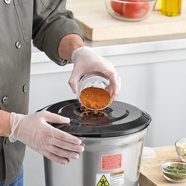 A person in gloves pouring a mixture of green spices into an AvaMix heavy-duty food blender.