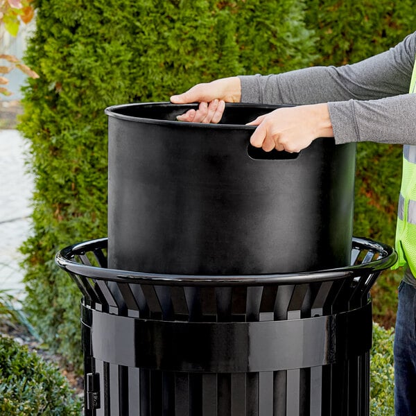 A man putting a Lancaster Table & Seating black plastic round can liner in a trash can.
