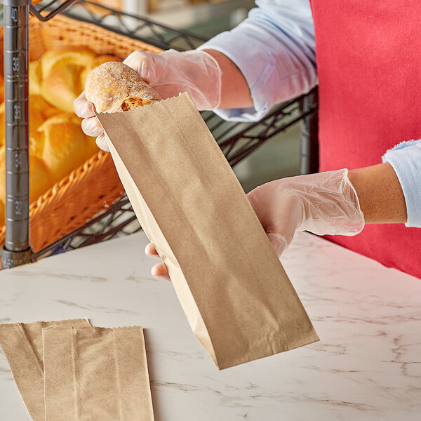 A person in gloves holding a brown Kraft bread bag.