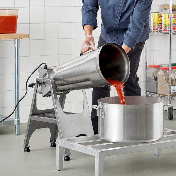 A man pouring red liquid into a large metal container on a metal table.