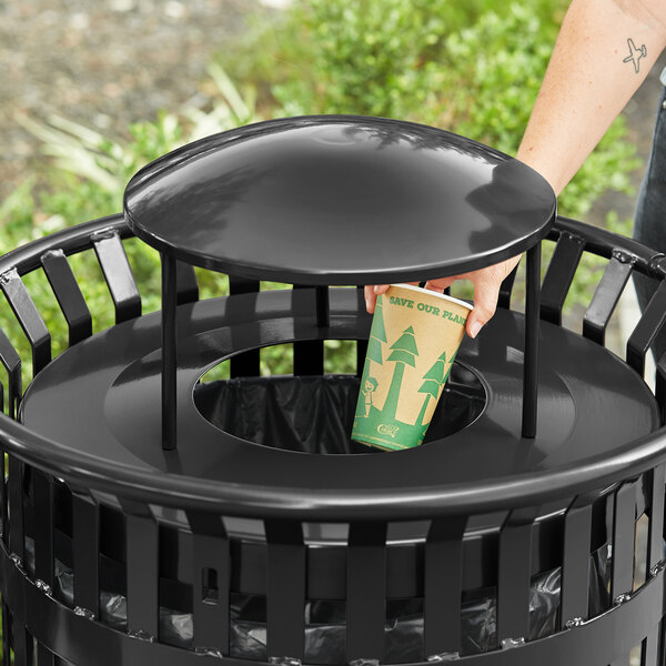 A hand putting a cup into a black round trash can lid.