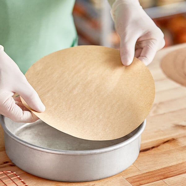 A person in gloves placing a Baker's Lane round parchment liner in a metal pan.