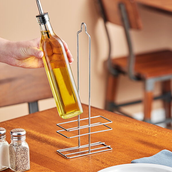 A hand pouring olive oil into a metal cruet rack.