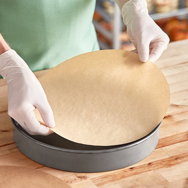 A person in gloves using a circular piece of Baker's Lane parchment paper.