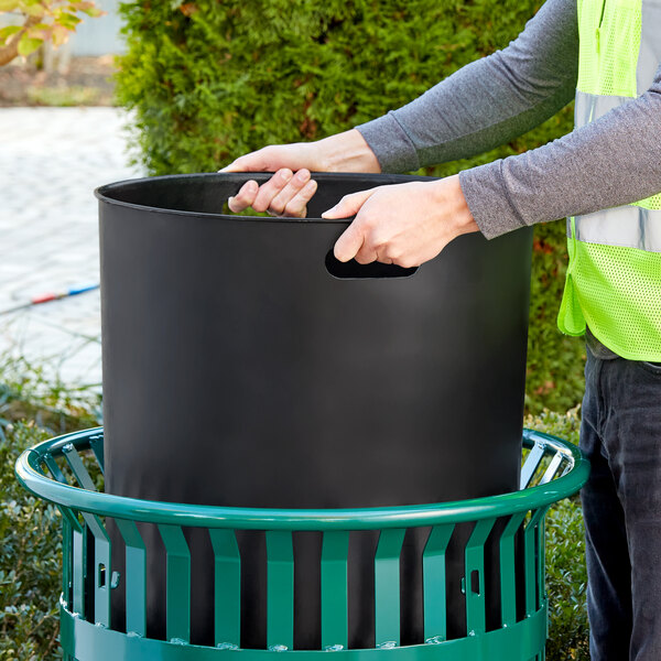 A person putting a Lancaster Table & Seating black plastic can liner in a trash can.