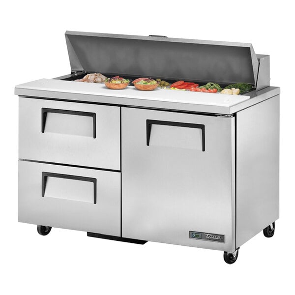 A True refrigerated sandwich prep table with left door and two drawers on a counter with food.