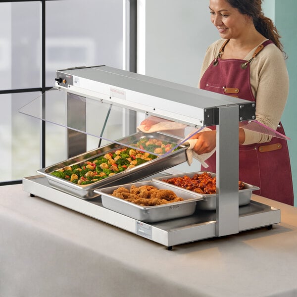 A woman wearing a red apron putting fried chicken into a ServIt heated buffet warmer.