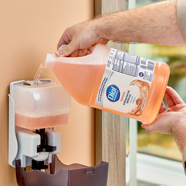 A person pouring Dial antibacterial hand soap into a soap dispenser.