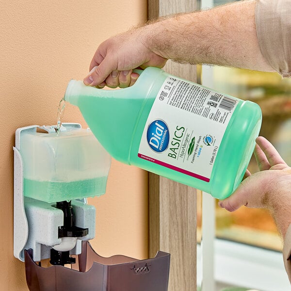 A person pouring Dial Professional Basics hypoallergenic foaming hand wash from a green gallon bottle into a soap dispenser.