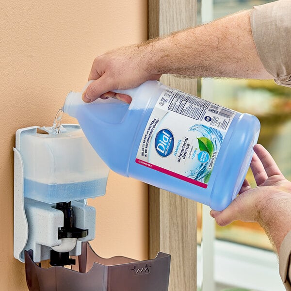 A hand pouring blue Dial Spring Water foaming hand wash from a large plastic container.