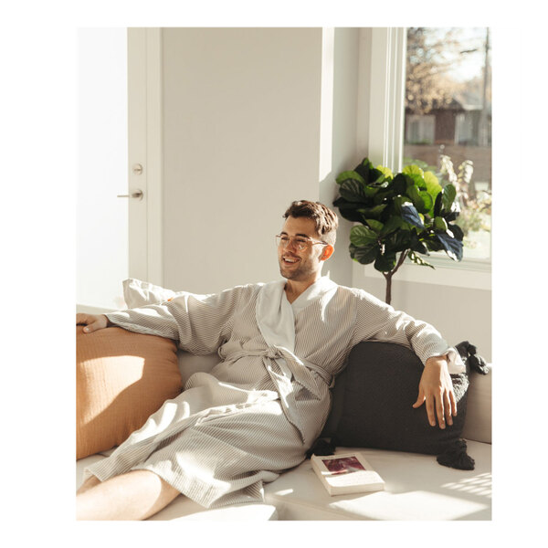 A man wearing a Telegraph Hill taupe seersucker bath robe sitting on a couch.