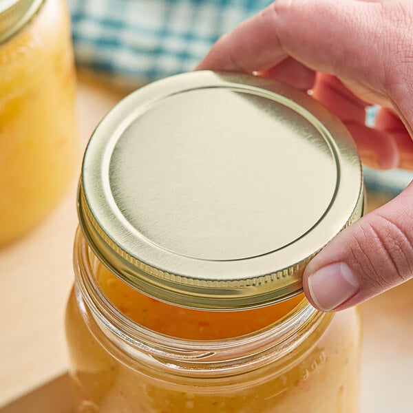 A person holding a jar with a gold metal lid containing yellow liquid.